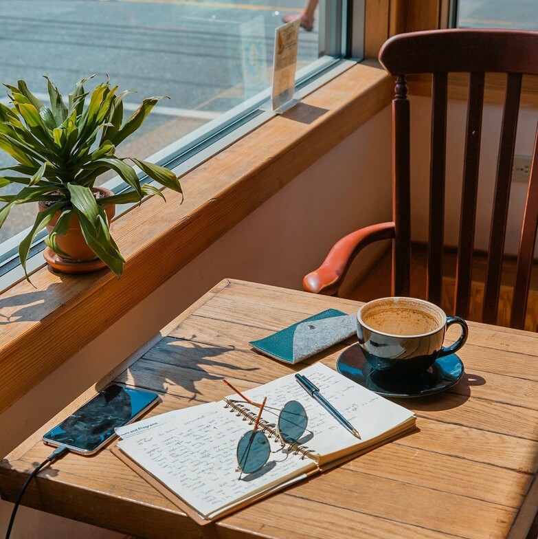 Journal, pen, and coffee on a café table, symbolizing self-reflection and intentional life planning