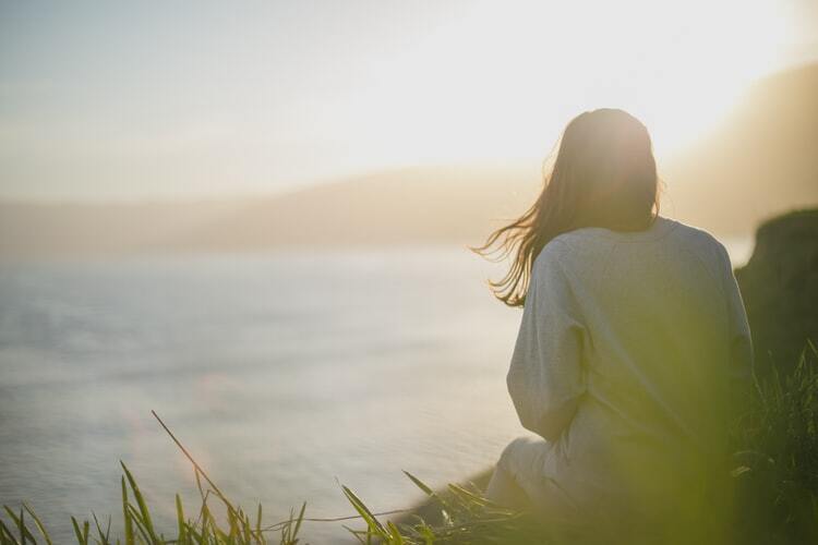 Woman seated alone, looking out over a quiet landscape