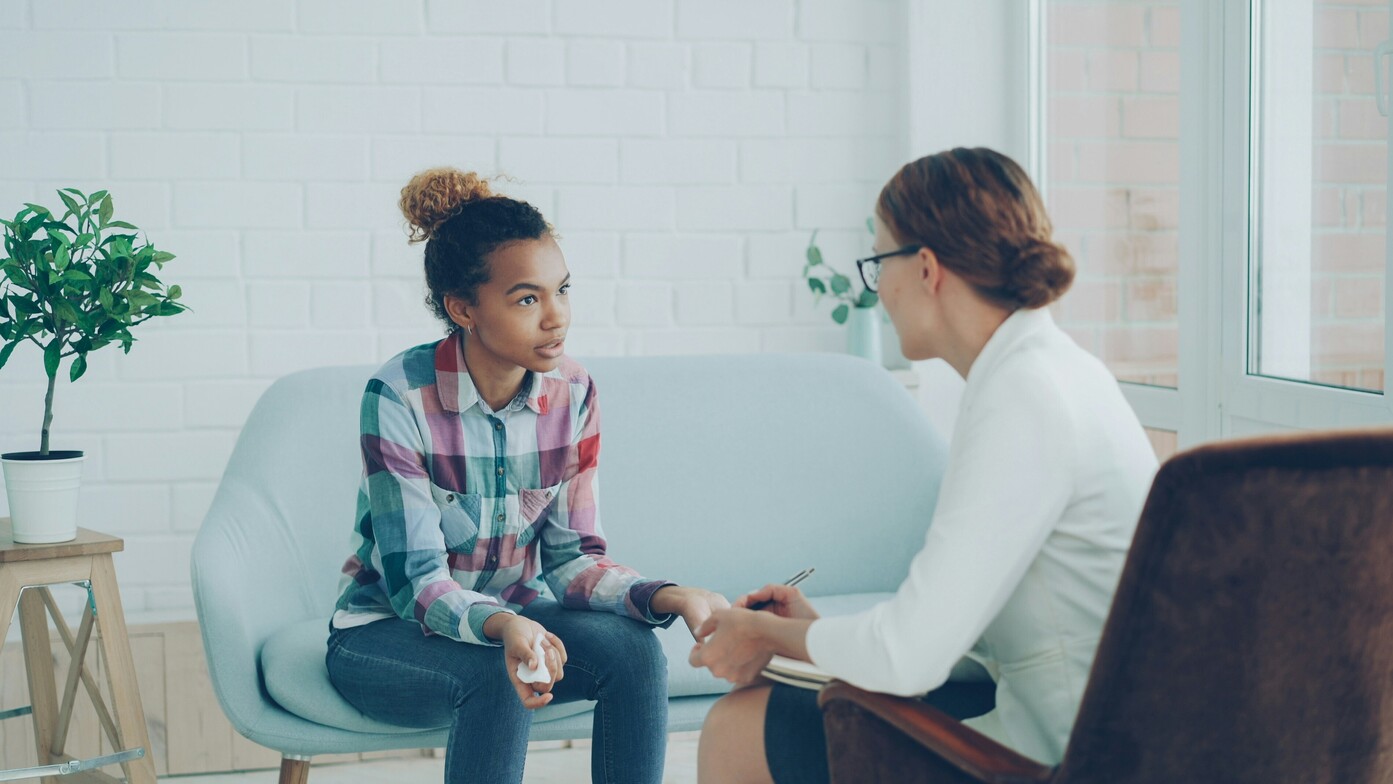 Woman sitting on a couch, speaking thoughtfully with her therapist during a counseling session.