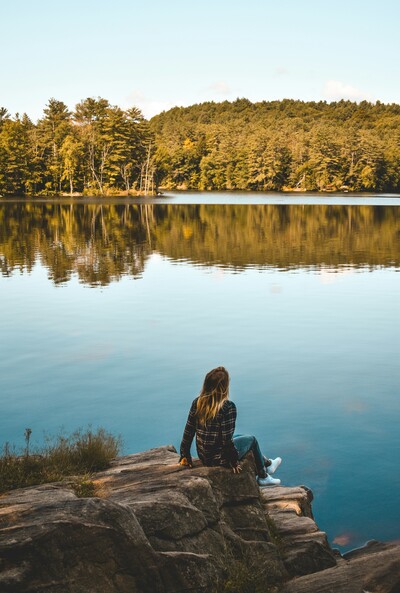 Person sitting by a calm lake, reflecting and taking in nature, representing ongoing therapy and emotional processing over time