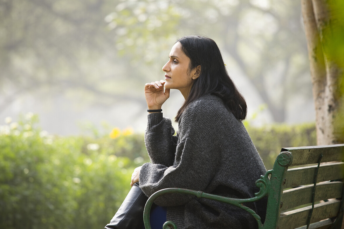 Woman sitting on a bench outdoors in quiet reflection, representing deep emotional processing in therapy