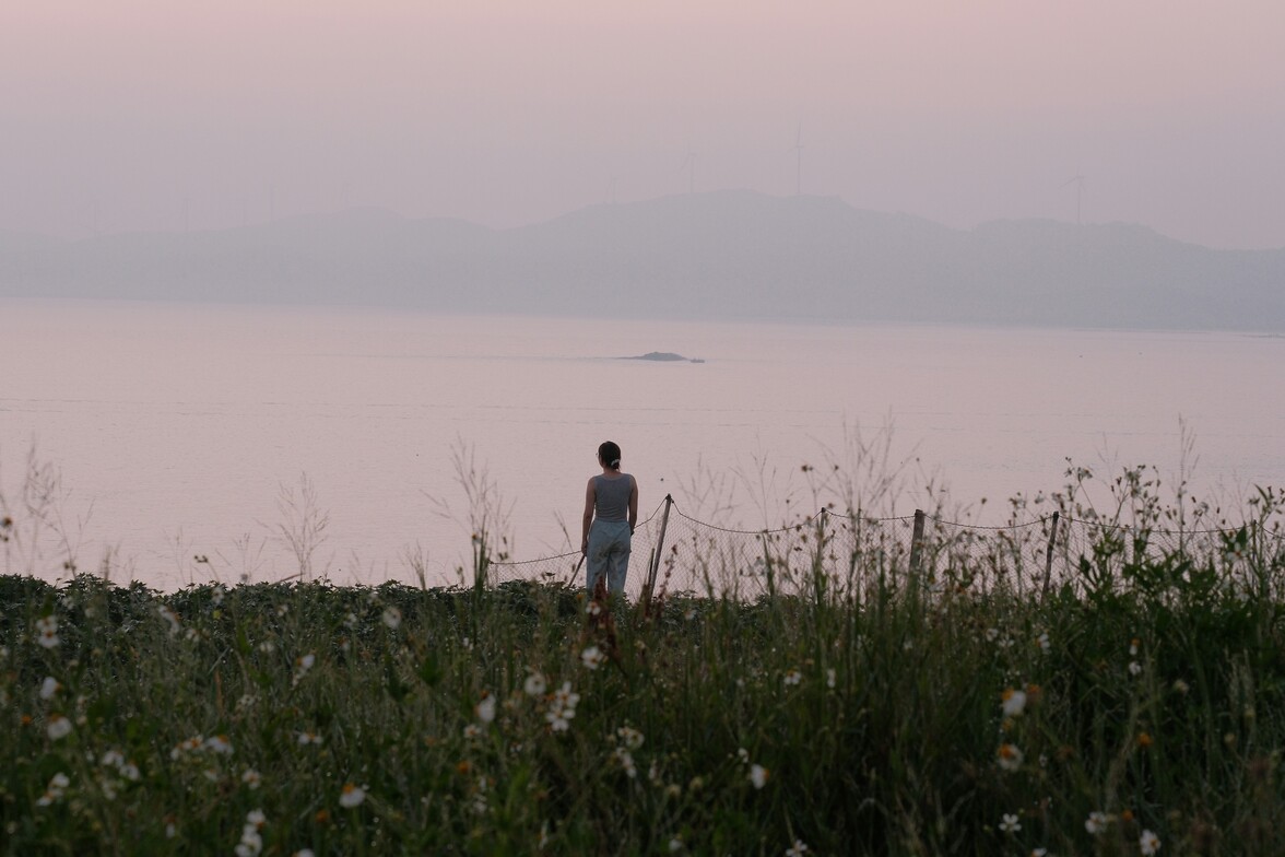 Person standing by a lake at sunset in quiet reflection, symbolizing meaning and purpose in therapy