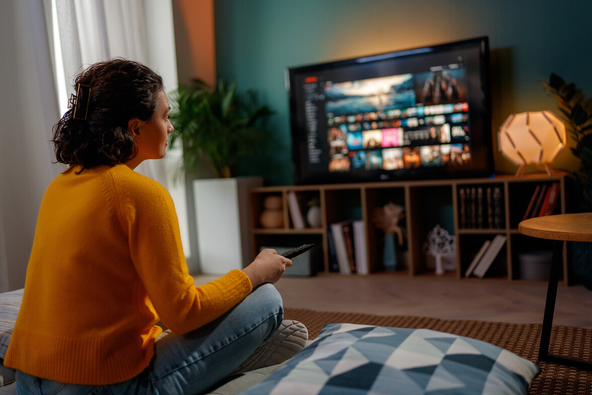 Person sitting on the floor in a cozy living room watching television after a long day, illustrating passive forms of rest and burnout recovery.
