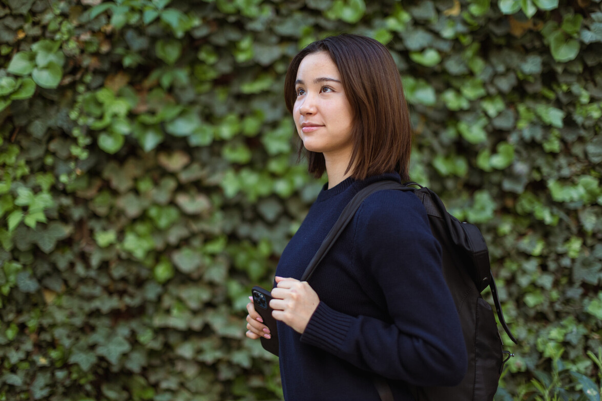 woman walking with backpack against green foliage