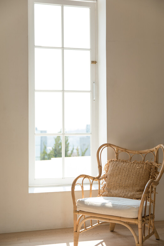 A rattan chair by the window through which the bright morning light shines