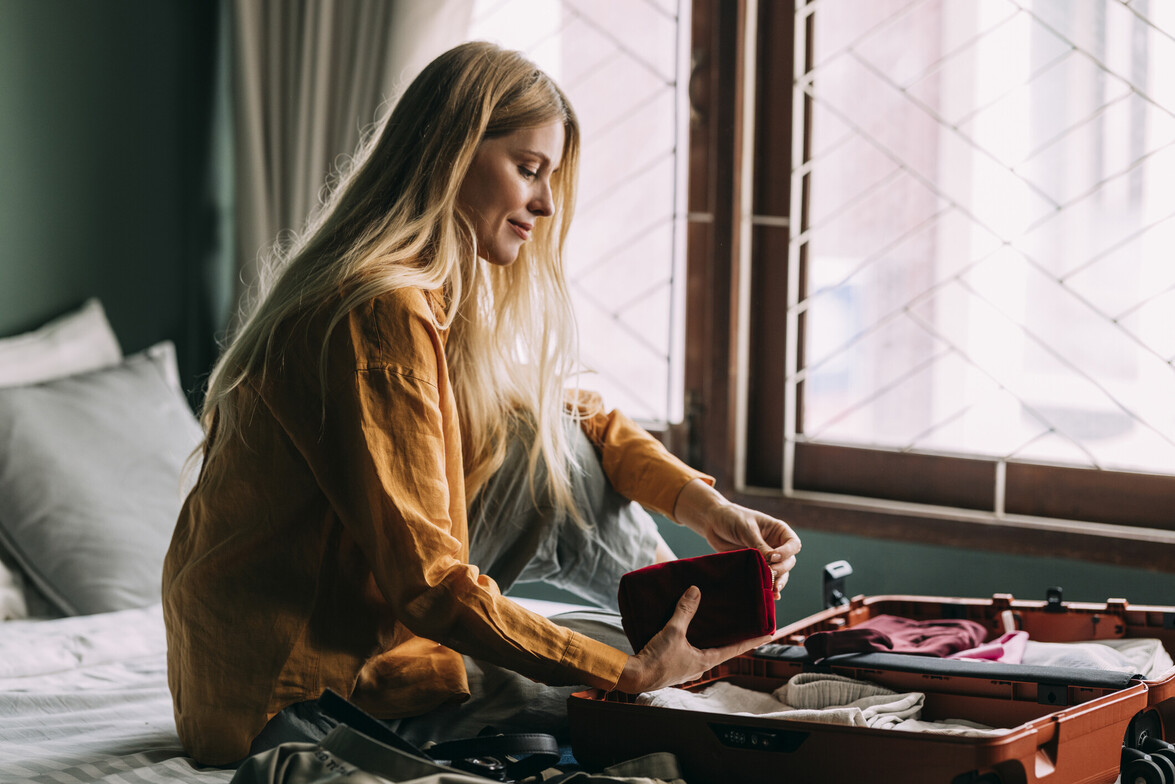 Woman sitting beside a window with an open suitcase, looking down at its contents