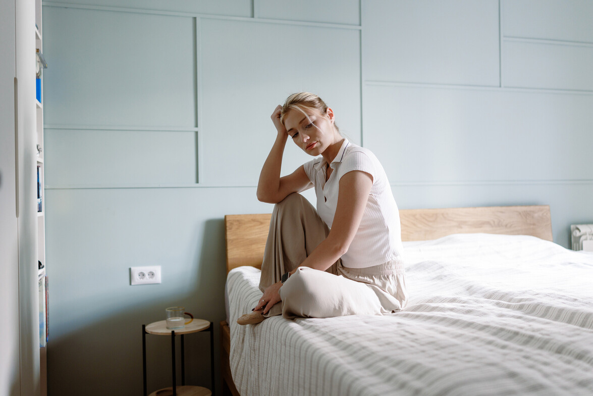 Young woman sitting on bed with hand on head